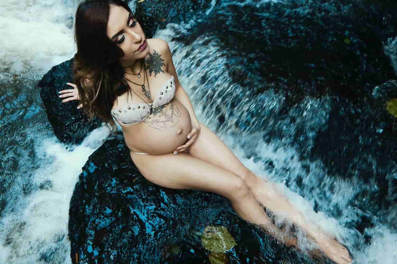 pregnant woman sitting on a rock surrounded by water