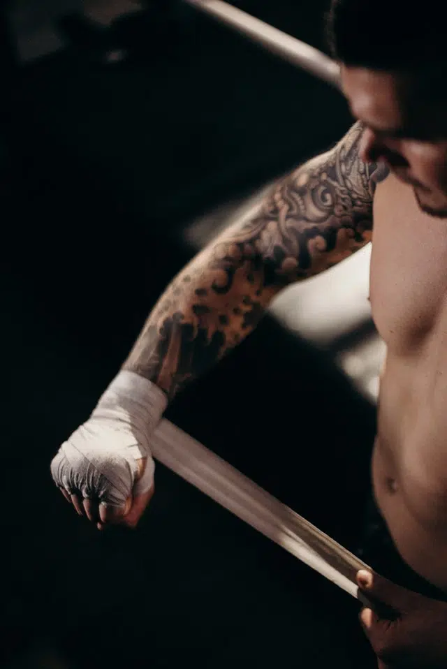 Man with tattoo on his right arm wraps his hand up in preparation for a spar