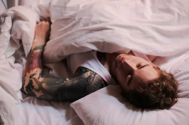 Man with arm sleeve tattoo sleeps on beige colored sheets
