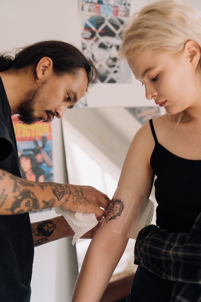 Tattoo artist wrapping female client's tattoo with saniderm for proper tattoo care first 48 hours