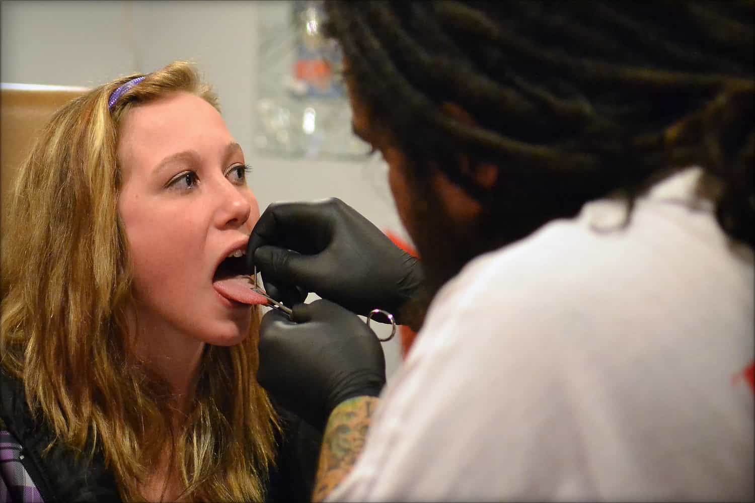 woman gettimg a snake eyes tongue piercing