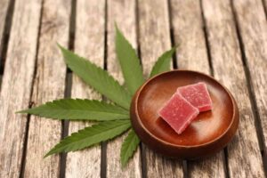 weed edible on a brown coaster on top of a cannabis plant leaf that is on a brown wooden table