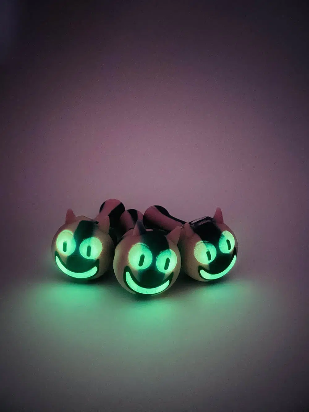three pink smiling cheshire cat pipes glowing from eyes and mouth and casting green and pink glow