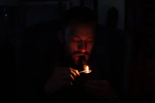 Young man lighting smoking pipe in darkness