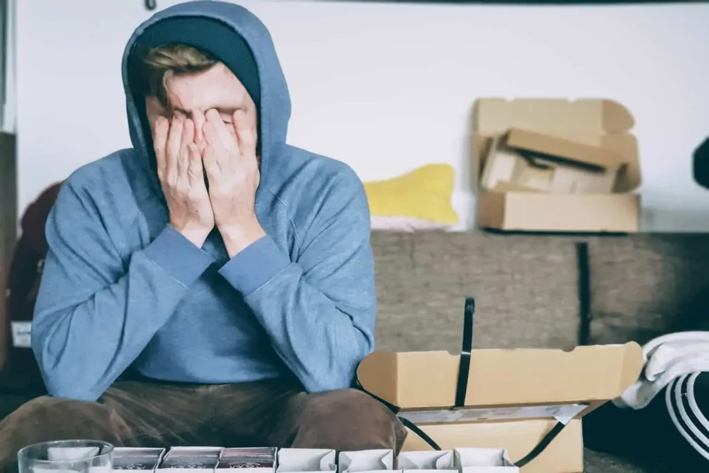 man in blue hoodie with hands over his face