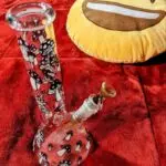 mushroom house bong on bed with red blanket and yellow smiley face pillow