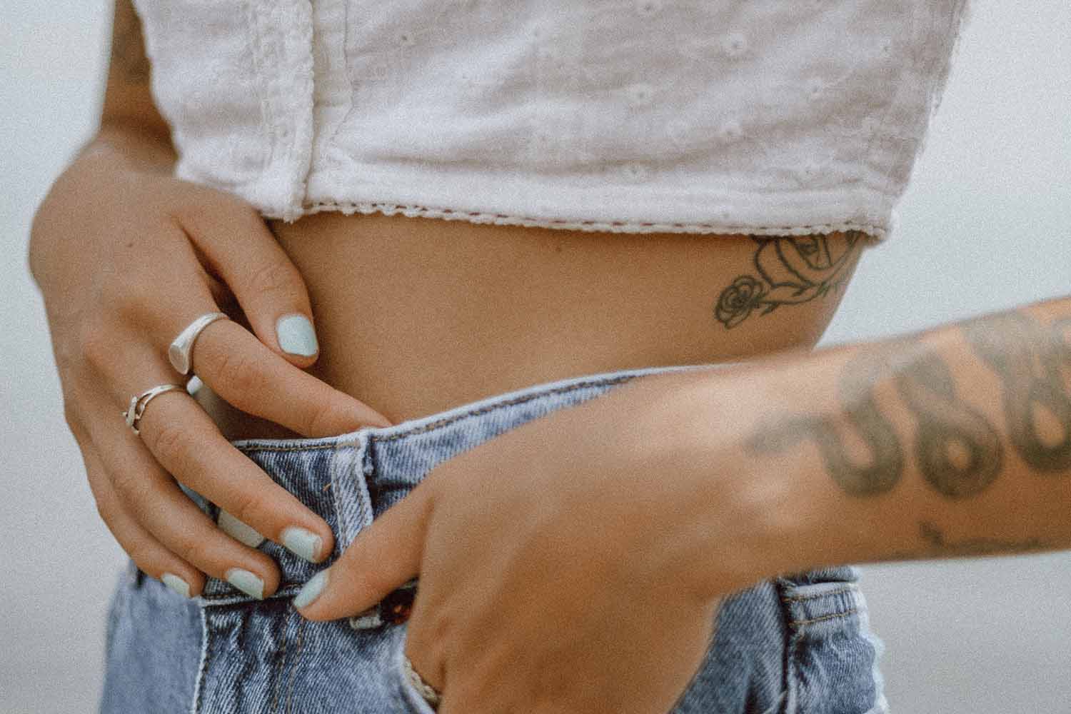 closeup of woman with tattoos and white shirt placing hand over stomach