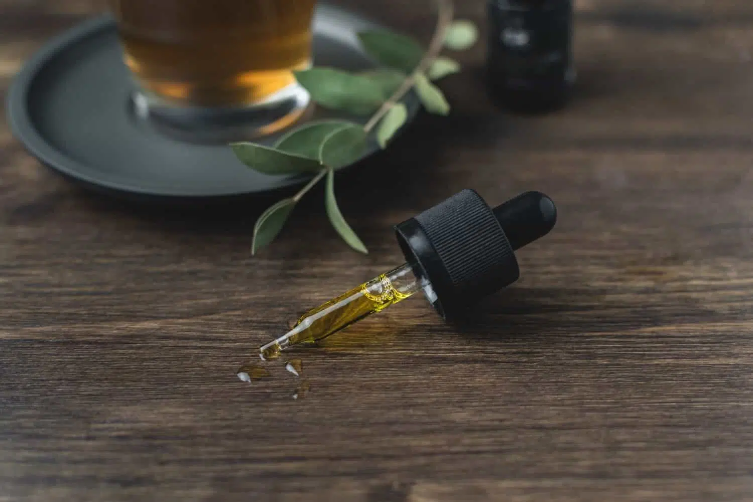 dropper with CBD oil on a wooden table with a glass of tea and leaves