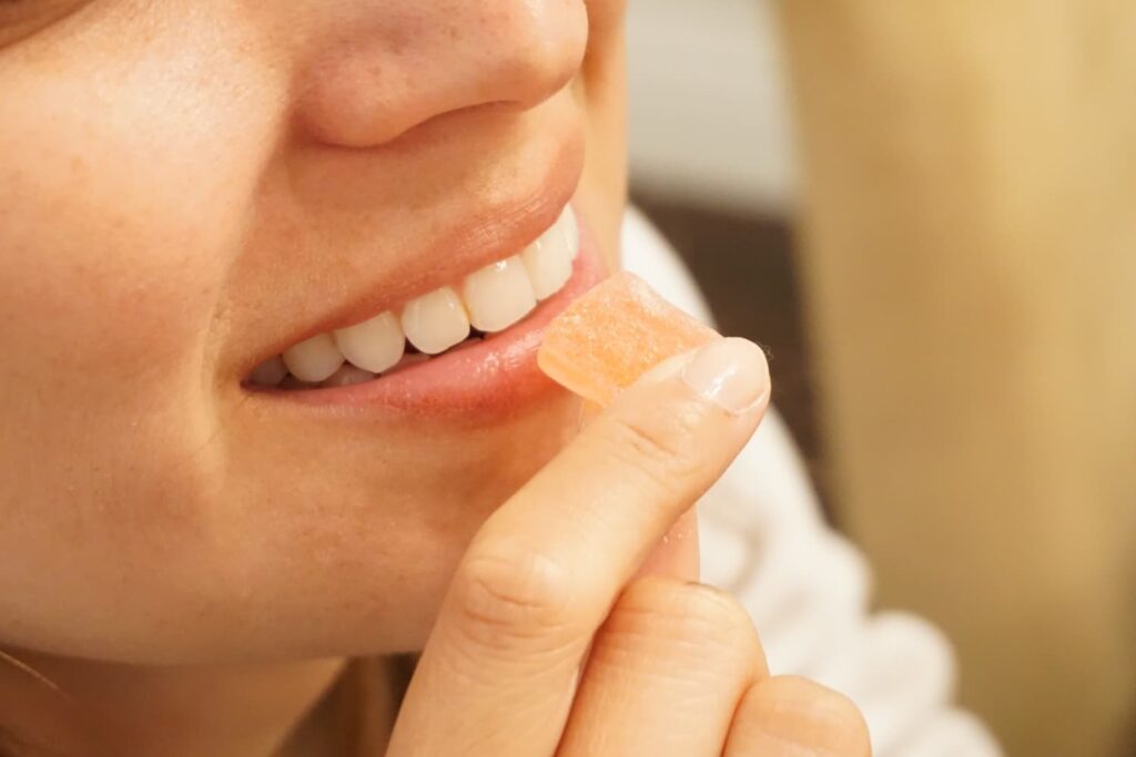 woman about to eat a square light orange gummy edible