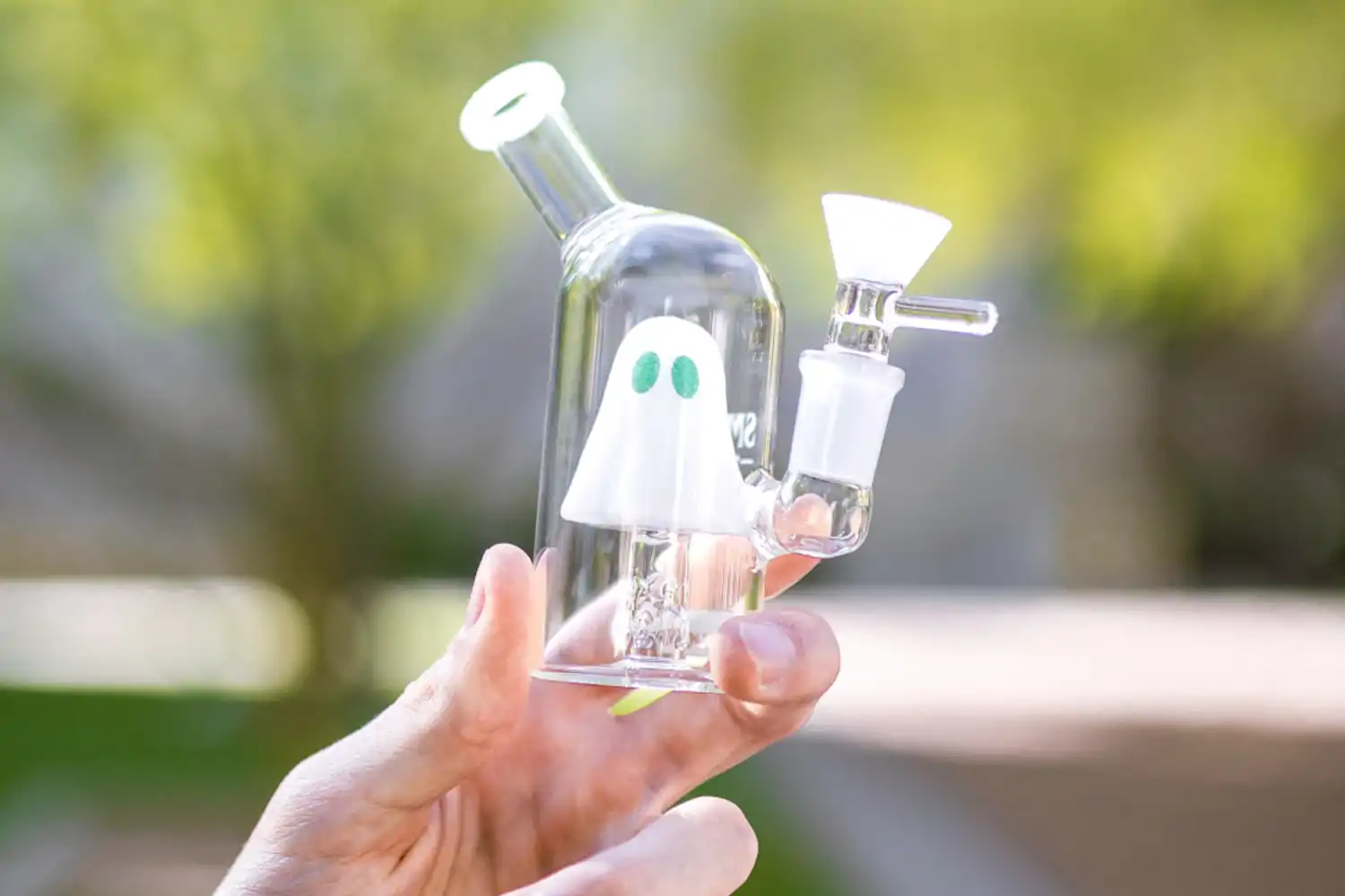 A person holding up a tiny bong with a ghost inside it
