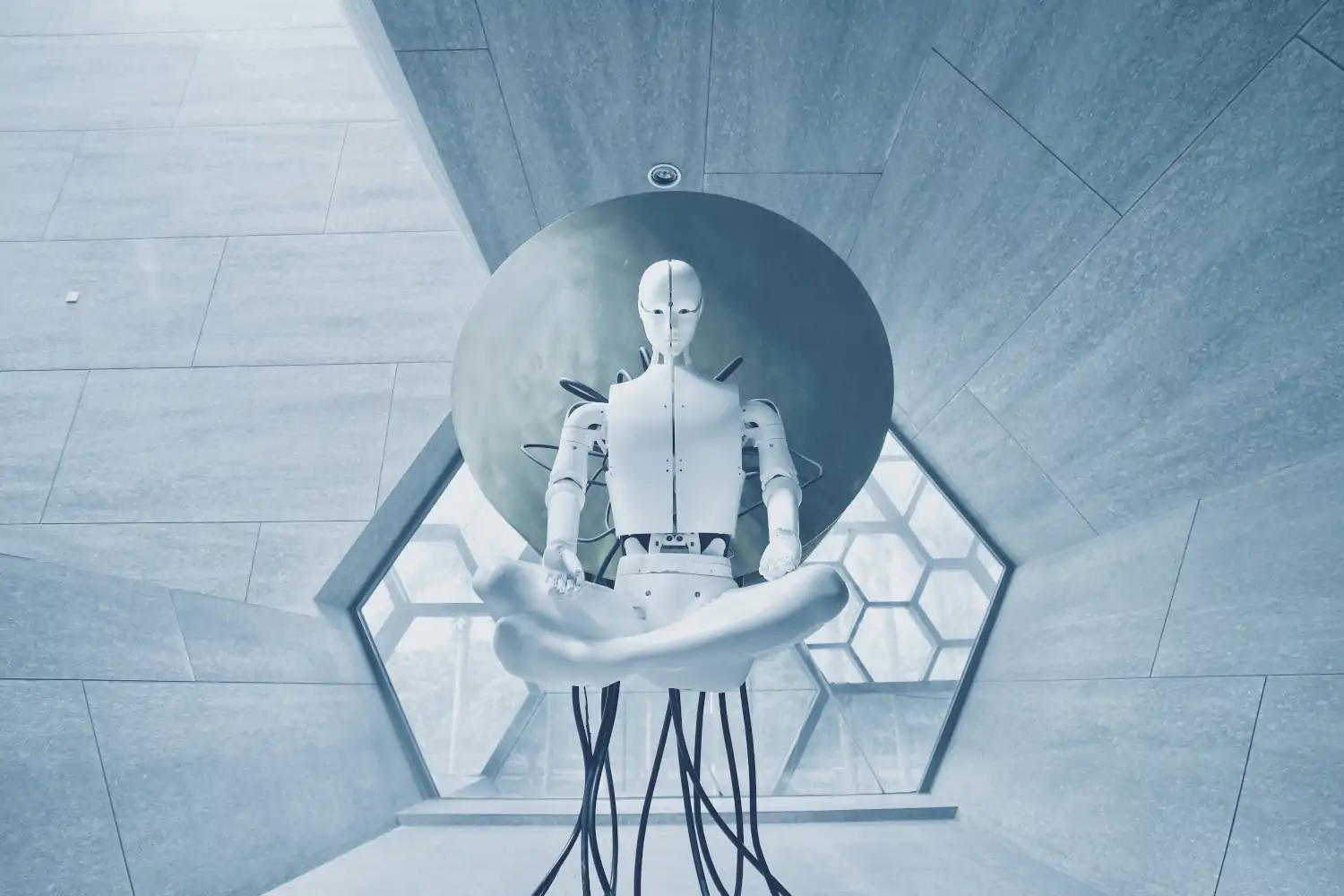 A white humanoid robot floats atop a throne of black wires in a grey room