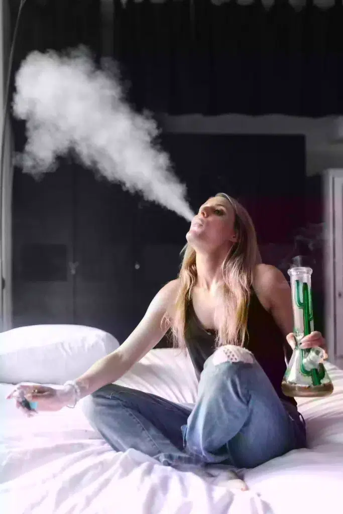 A person using a bong while sitting on a bed