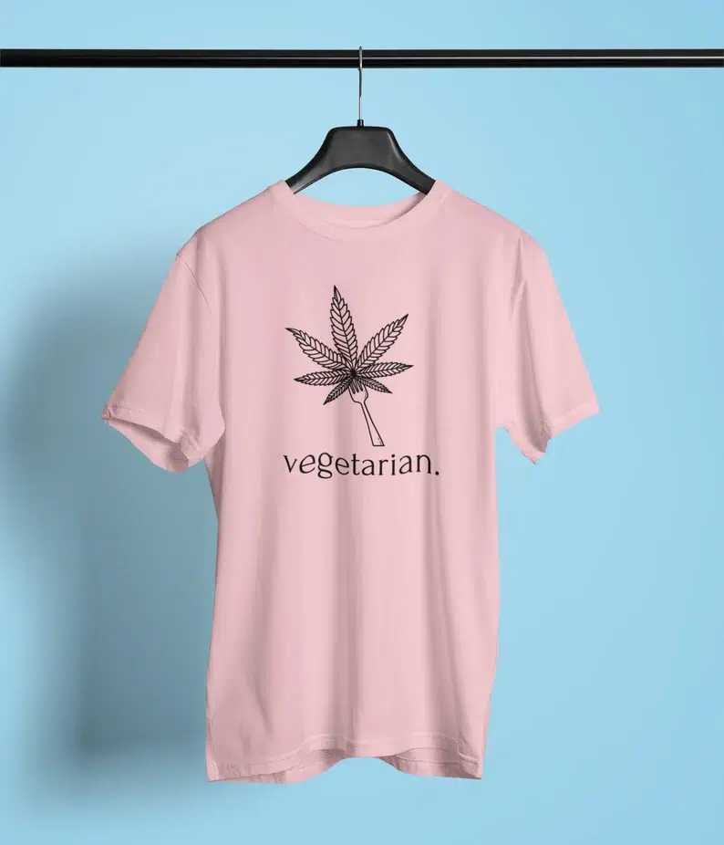 Pink t-shirt that says "Vegetarian" beneath a drawing of a weed leaf on a fork