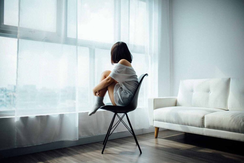 Frau sitzt auf einem Stuhl und schaut aus dem Fenster