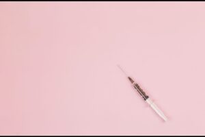 syringe for administering botox injections on pink background