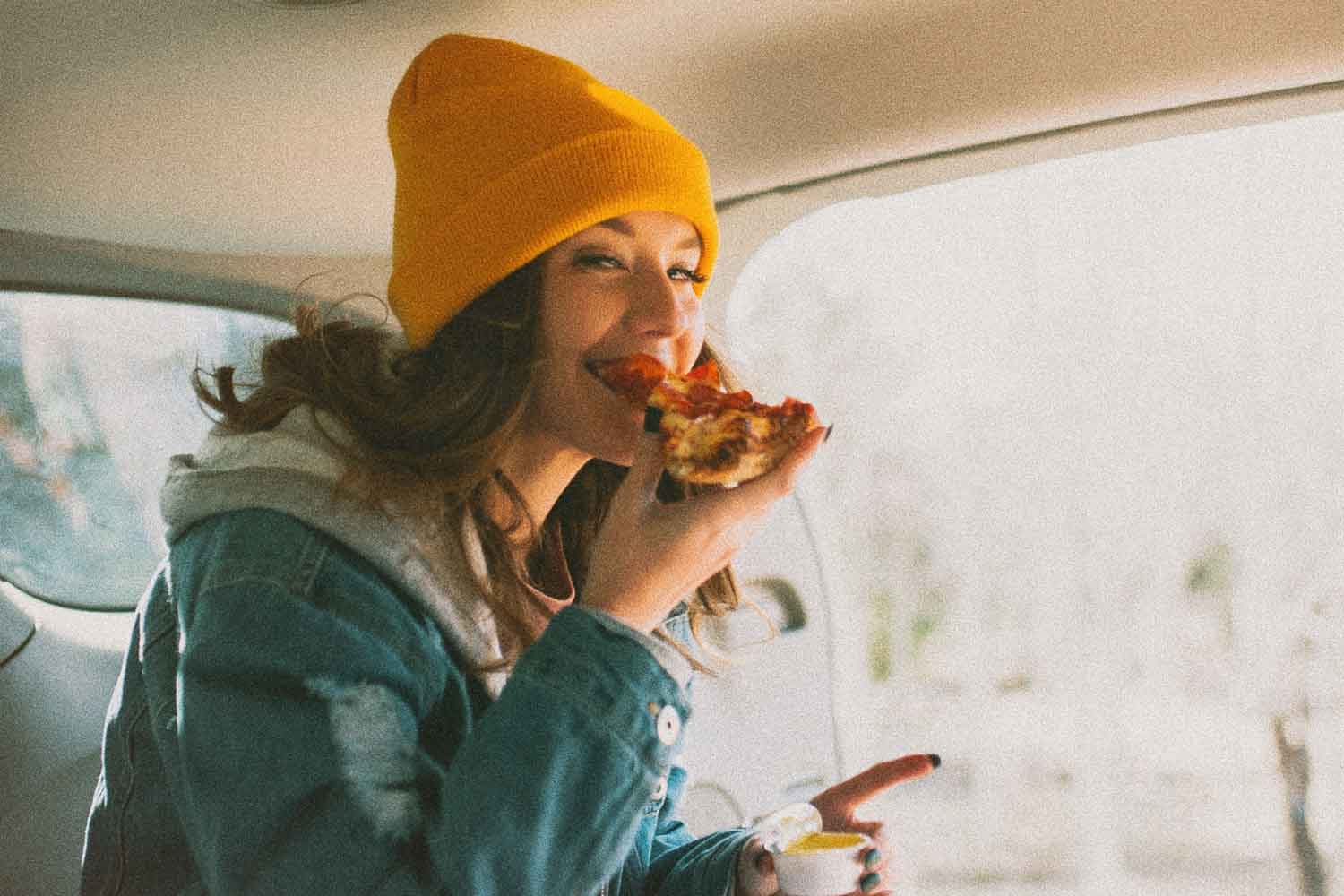 woman eating pizza in car