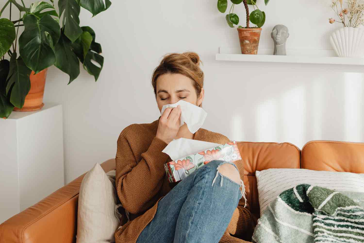 woman sitting on couch blowing nose allergies