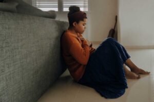 woman having a panic attack on floor behind sofa holding heart