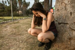 woman having sensory overload from weed sitting next to tree to calm down