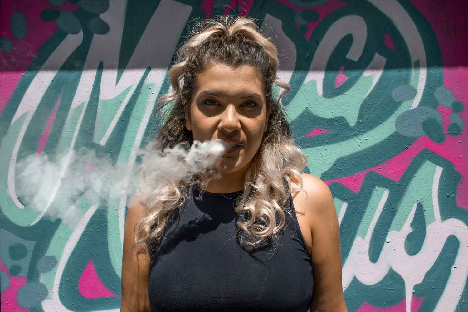 woman smoking weed in front of graffiti
